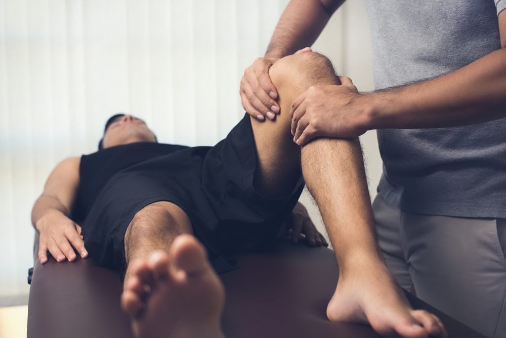 Fysioterapeut undersøger knæ på mand med knæsmerter